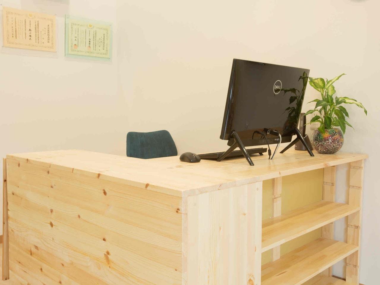 「木の温もりある受付カウンターで次回予約を案内する清潔な空間（上福岡みつばち美容整骨院）」